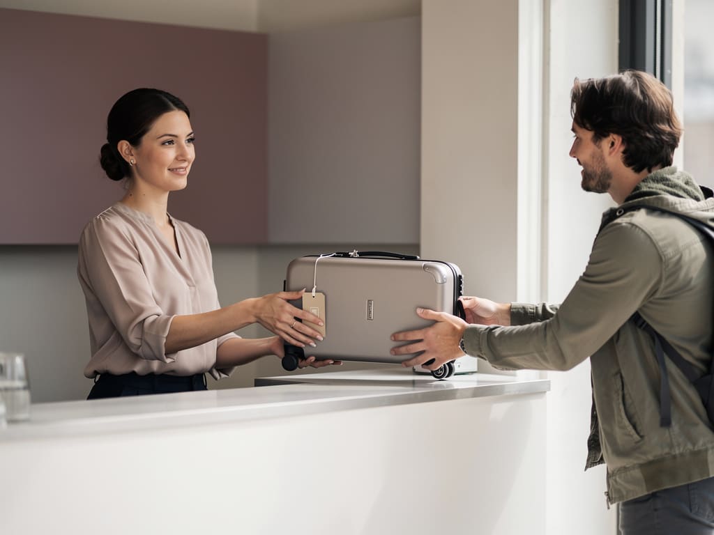 Operatore che consegna una valigia etichettata a un viaggiatore al banco